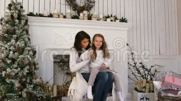 年轻的母亲和她的女儿在壁炉旁的椅子上感到舒服视频的预览图