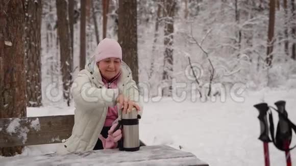 冬木中的养老人这位老妇人坐在长凳上休息准备用热水瓶泡热茶视频的预览图