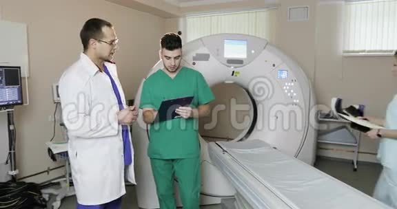 4两位穿着医疗服的年轻医生在一家诊所的橱柜CT扫描仪里交谈视频的预览图