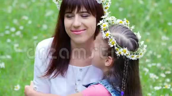夏天在森林里的一片洋甘菊的草地上一个年轻的女人一个黑发女人一个七岁的女孩母女编织着视频的预览图