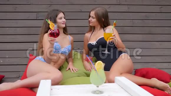 穿着泳衣的女朋友喝着饮料坐在五颜六色的垫子上参加母鸡聚会穿着泳衣的女孩子喝着鸡尾酒视频的预览图