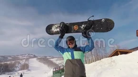 站在滑雪公园里的成年胡须男他举起一块滑雪板表示他今天很高兴他衣着热情视频的预览图
