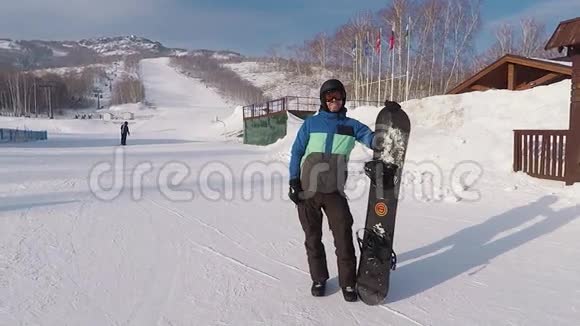 欢乐的滑雪板站在他刚刚从山上下来的背景上把他的滑雪板年轻人视频的预览图