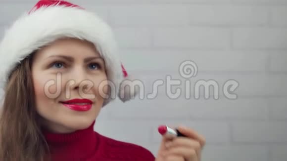 新年快乐圣诞女孩在玻璃字上写口红新年快乐戴帽子的漂亮女孩发信息视频的预览图