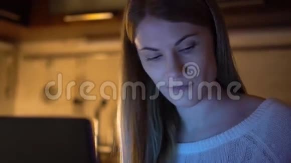 美丽迷人的女人浏览互联网和笔记本电脑晚上厨房吃薯条视频的预览图