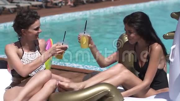 女朋友在泳池边的床垫上晒日光浴喝着清爽的鸡尾酒穿泳衣的漂亮年轻女孩视频的预览图