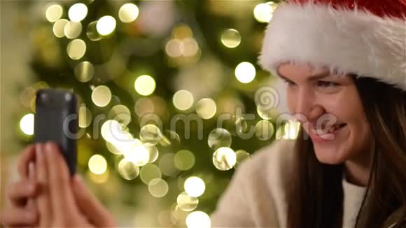 圣诞帽中的快乐女人做自拍在圣诞树背景下庆祝圣诞节特写肖像画视频的预览图