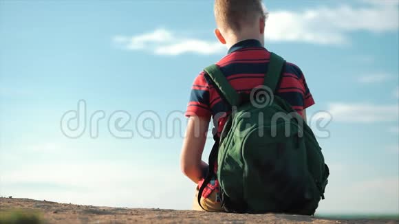 一个穿着红色衬衫背着背包的少年夕阳西下坐在高高的小山上望着云层视频的预览图