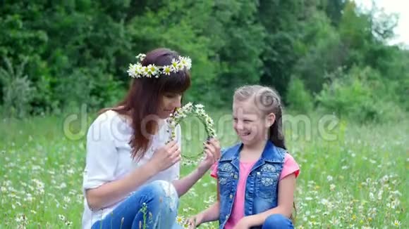 夏天在森林里的一片洋甘菊的草地上一个年轻的女人一个黑发女人一个七岁的女孩母女编织着视频的预览图