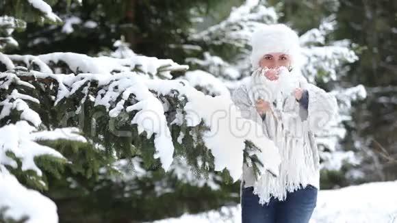 针织毛衣和皮帽穿着迷人的女性把雪球扔进照相机视频的预览图