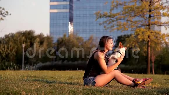 日落时分美丽的女孩和一只狗坐在公园里视频的预览图