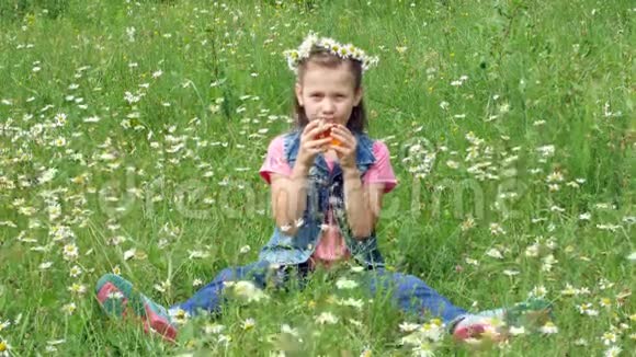 在一片洋甘菊的草坪上一个戴着洋甘菊花圈的甜美女孩从杯子里喝着洋甘菊茶笑得很漂亮视频的预览图