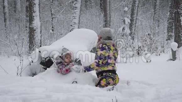 冬天在树林里女孩和孩子一起在树林里度过时光小女孩在雪堆里婴儿没有心情视频的预览图