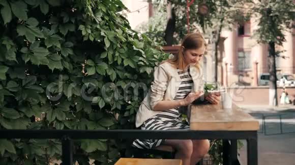 在户外城市咖啡厅午休时使用平板电脑的女人年轻微笑的女孩坐在平板电脑和视频的预览图