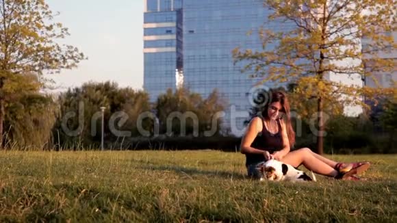 日落时分美丽的女孩和一只狗坐在公园里视频的预览图