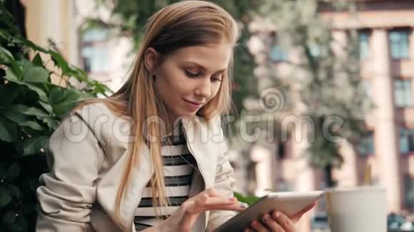 在户外城市咖啡厅午休时使用平板电脑的女人年轻微笑的女孩坐在平板电脑和视频的预览图