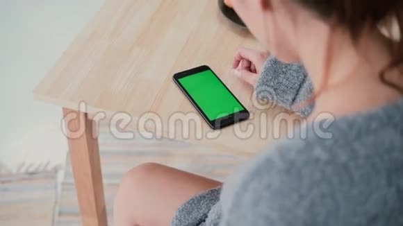 在厨房里坐在餐桌前的女人的后景布鲁内特女孩使用智能手机绿色屏幕视频的预览图