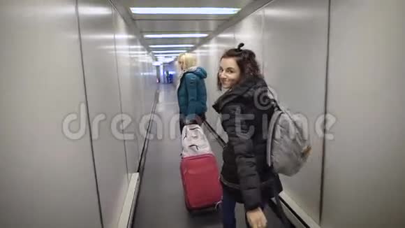 机场两个年轻女人在你的航班上奔跑金发女孩带着一个手提箱匆忙地穿过管子到视频的预览图