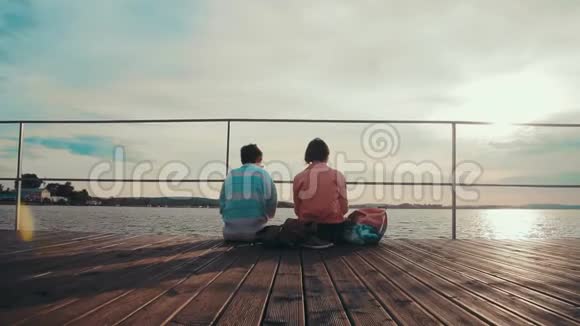 两个女朋友坐在木墩边的池塘边放松快乐的夏日朋友视频的预览图