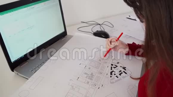 设计工程师坐在她办公室的办公桌前在笔记本电脑上打字在她的办公桌上放蓝图视频的预览图