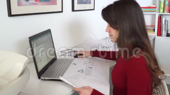 设计工程师坐在她办公室的办公桌前在笔记本电脑上打字在她的办公桌上放蓝图视频的预览图