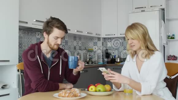 年轻夫妇在早餐时男人在智能手机上展示一些东西他的女朋友视频的预览图