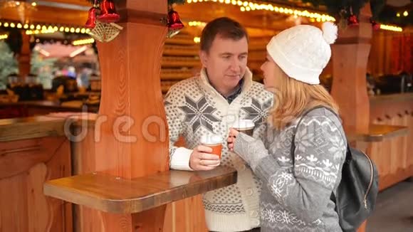 一对快乐的夫妇穿着暖和的衣服喝着咖啡在圣诞市场上聊天圣诞快乐新年快乐视频的预览图