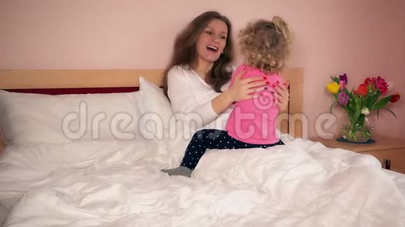 微笑妈妈和她可爱的女儿在床上玩得很开心视频的预览图