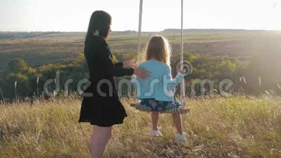 年轻的母亲和她的孩子女儿在秋千上荡秋千在户外度过了一个温暖的秋天快乐的爱视频的预览图