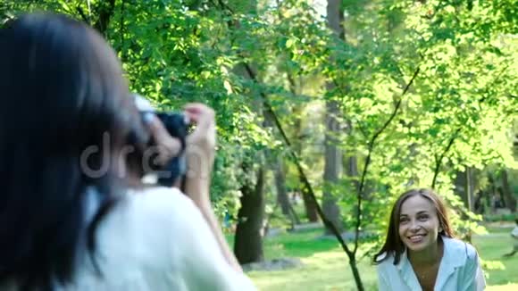 一位穿着白色衬衫的漂亮女孩职业摄影师正在一个公园里用柔软的衣服拍一个快乐的微笑女孩的照片视频的预览图