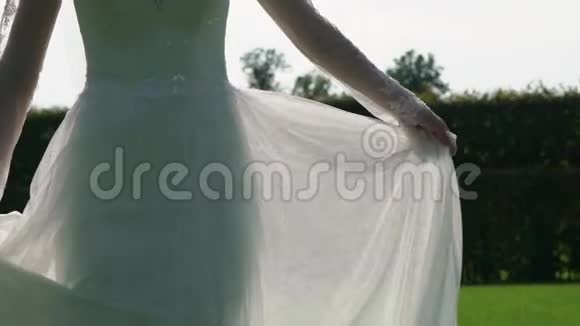 年轻的新娘穿着华丽的婚纱挥舞着飞行织物时尚的女性在公园里摆姿势视频的预览图