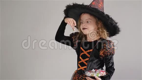 穿着黑色橙色连衣裙和大帽子的女孩女孩手里拿着糖果不给糖就捣蛋万圣节派对视频的预览图