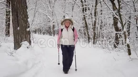 精力充沛的女人穿着温暖的白色背心带着引擎盖和黑色裤子悠闲地与活跃的北欧散步在一起视频的预览图
