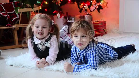 圣诞快乐可爱的小男孩和他美丽的妹妹孩子们在圣诞节附近躺在地板上笑着视频的预览图