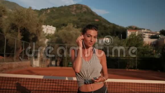 夏天美丽的女人正在网球场上戴着耳机跳舞视频的预览图