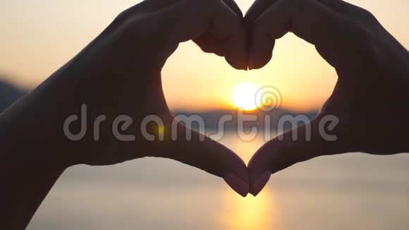 年轻女性手的剪影使心脏形状在海洋背景与美丽的日落夏季概念视频的预览图