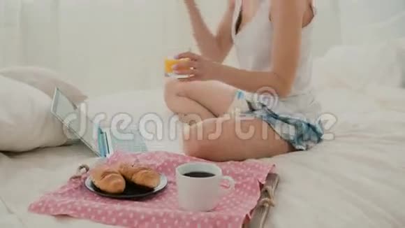 年轻迷人的女人在床上喝果汁布鲁内特女孩在早餐时上网使用笔记本电脑视频的预览图