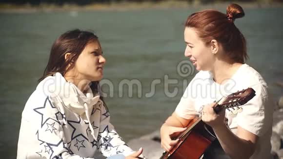 两个女朋友在河岸上休息唱歌弹吉他视频的预览图
