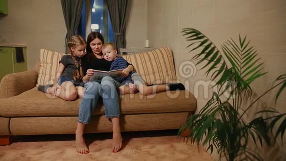 妈妈和他的女儿和小儿子一起坐在沙发上一边在沙发上看故事视频的预览图