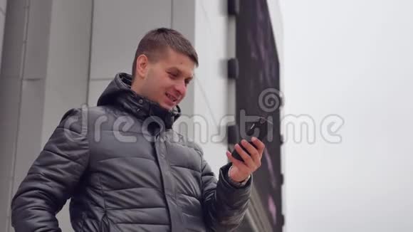 男人微笑相机城市自拍照片你的智能手机在冬天的男人户外视频的预览图