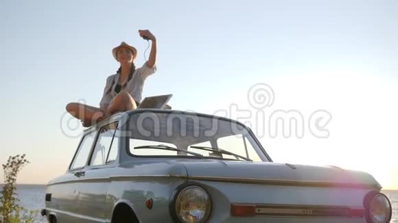 照片自拍在车上女孩坐在屋顶复古车背光做自拍在电话上年轻女子使用太阳能视频的预览图