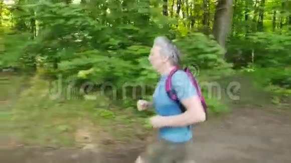 穿着蓝色t恤背包在森林里奔跑慢动作视频的预览图