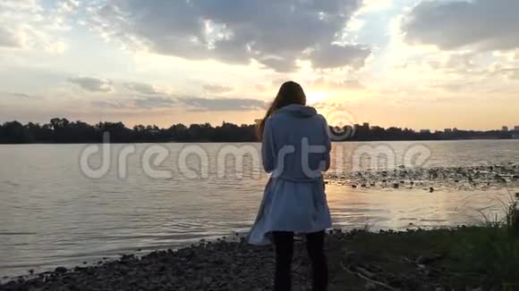 年轻的孕妇站在夕阳下美丽的河岸上视频的预览图