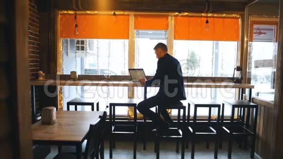 自信的年轻人穿着休闲装在笔记本电脑上工作而坐在创意办公室或咖啡馆的窗户附近视频的预览图