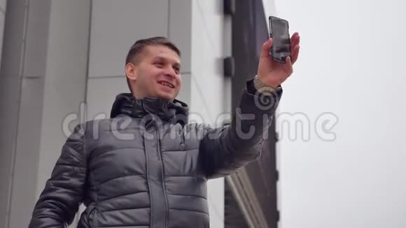 男人微笑相机城市自拍照片到你的智能手机在冬天的男人户外视频的预览图