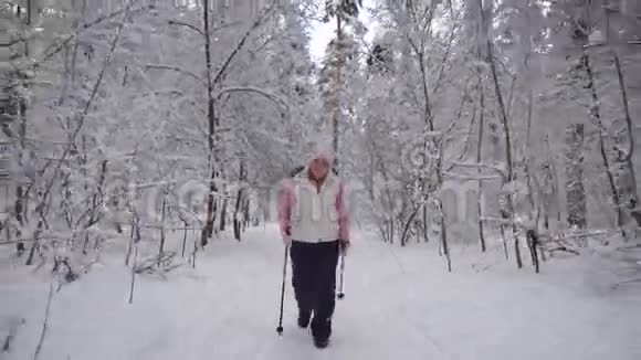 穿着时髦的老年妇女从事一种新型的运动在冬天的积雪覆盖的木材中行走在职养恤金领取者视频的预览图