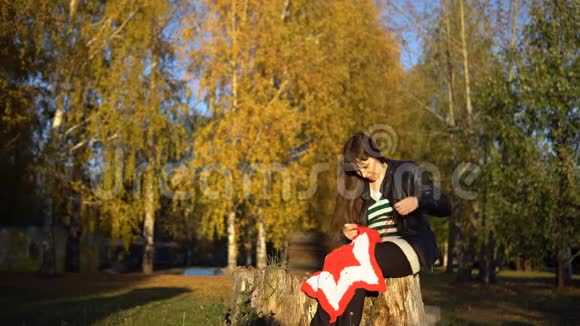 一个穿着皮夹克的年轻女人在公园里编织一条格子呢视频的预览图