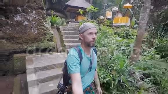 巴厘岛在岛上游览穿着蓝色衬衫肩上背着背包的人走在石头上视频的预览图