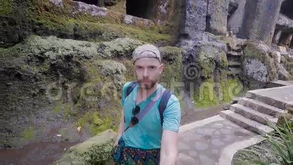 男性旅行者徒步探索古老的巴厘岛寺庙周围的环境手里拿着自拍棒有胡子的人视频的预览图