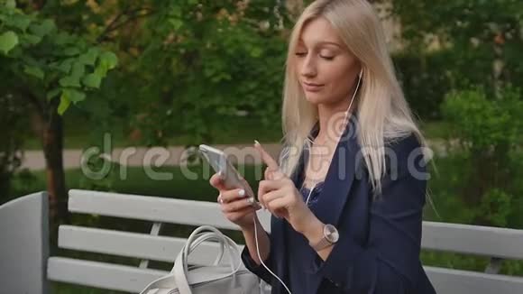 穿西装的年轻商务女性在智能手机上写信息一个漂亮的金发女郎正坐在长凳上用一个视频的预览图
